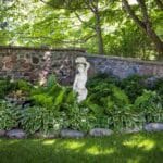 A beautiful backyard garden with different varieties of perennials and a statue.