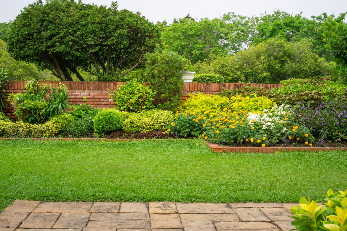 A beautiful backyard garden with a green lawn and a lot of shrubs and plants.