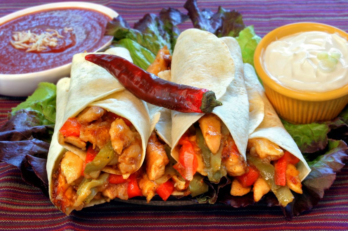 A bunch of chicken wraps with condiments and vegetables on a table.