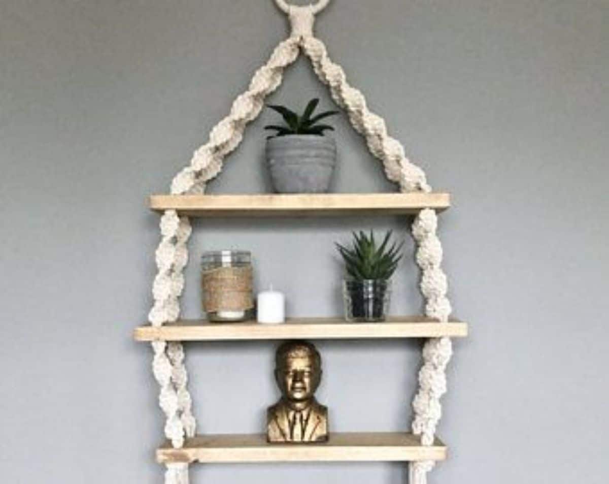 A macrame shelf with a statue, plants in pots, and other decors.