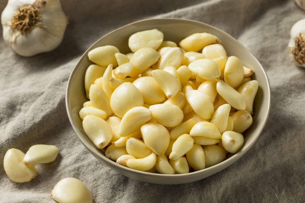 A white bowl full of peeled garlic cloves.